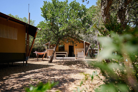 Tienda safari Villatent Nomad en Camping Leï Suves, Francia, rodeada de árboles y una hamaca afuera.