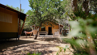 Tienda safari Villatent Nomad en Camping Leï Suves, Francia, rodeada de árboles y una hamaca afuera.