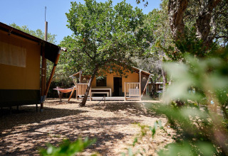 Tienda safari Villatent Nomad en Camping Leï Suves, Francia, rodeada de árboles y una hamaca afuera.