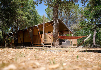 Safari tent Villatent Nomad with porch and hammock at Camping Leï Suves in France, surrounded by lush trees.