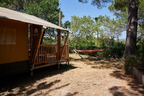 Tienda safari Villatent Nomad con porche y hamaca en un entorno natural en Camping Leï Suves, Francia.
