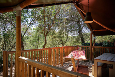 Terrazza in legno con amaca e tavolo in una tenda safari al Camping Leï Suves, Francia.