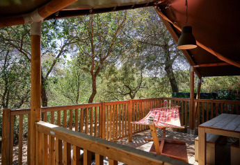Terraza de madera con hamaca y mesa en una tienda safari en Camping Leï Suves, Francia.