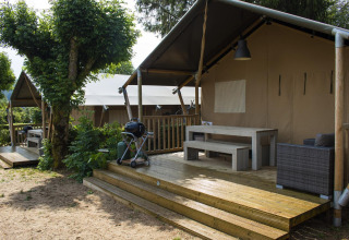 Tienda safari Villatent Nomad con terraza de madera y barbacoa en Camping Les Genêts, Francia, rodeada de naturaleza.