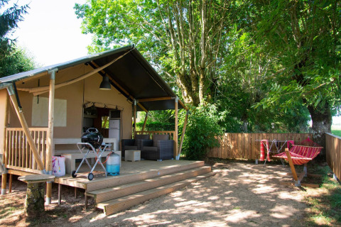 Tienda safari Villatent Nomad en Camping Les Genêts, Francia, con terraza de madera y hamaca al aire libre.