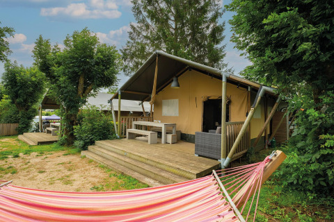 Tienda safari Villatent Nomad en Camping Les Genêts, Francia, con terraza de madera y hamaca colorida