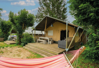Tienda safari Villatent Nomad en Camping Les Genêts, Francia, con terraza de madera y hamaca colorida