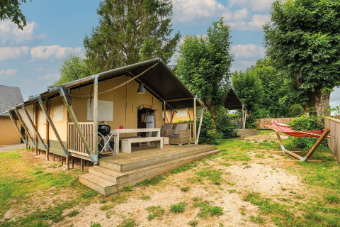 Tienda safari Villatent Nomad en Camping Les Genêts, Francia, con terraza, muebles y hamaca exterior.
