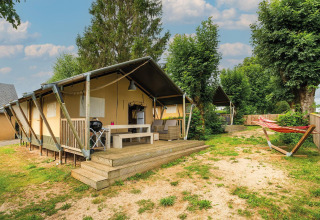 Safaritent Villatent Nomad bij Camping Les Genêts in Frankrijk met terras, tuinmeubels en een hangmat.