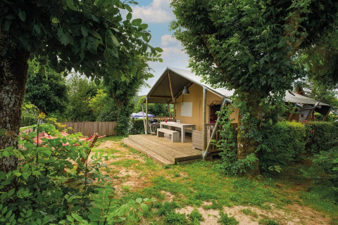 Tienda safari Villatent Nomad en Camping Les Genêts, Francia, rodeada de árboles y vegetación verde.