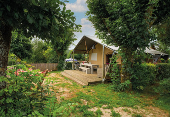Safari tent Villatent Nomad at Camping Les Genêts in France, surrounded by trees and a wooden terrace.