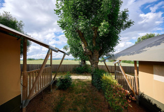 Blick von einem Villatent Nomad Safarizelt auf Camping Les Genêts in Frankreich mit Baum und Holzveranda.
