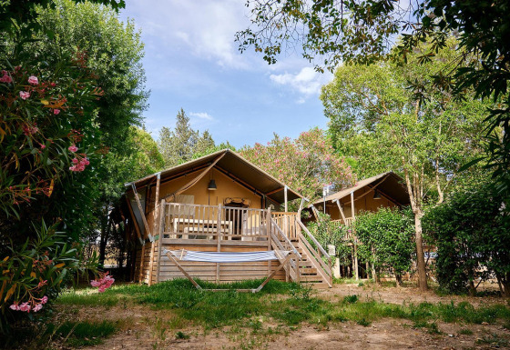 Zwei Safari-Zelte mit Veranda und Hängematte auf Camping Les Pêcheurs in Frankreich, von Bäumen umgeben.