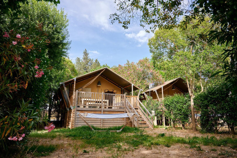 To safaritelte med store verandaer og hængekøje på Camping Les Pêcheurs i Frankrig, omgivet af grønt.