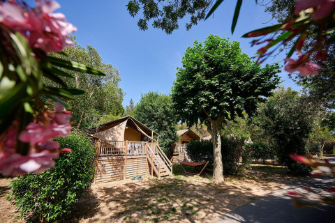Tienda safari Villatent Nomad en Camping Les Pêcheurs, Francia, rodeada de árboles verdes y flores coloridas.