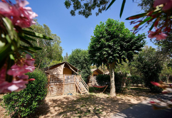 Tienda safari Villatent Nomad en Camping Les Pêcheurs, Francia, rodeada de árboles verdes y flores coloridas.