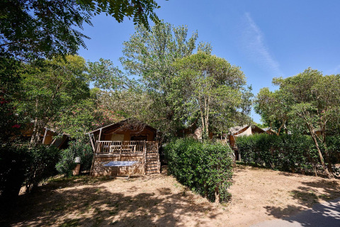 Tienda safari Villatent Nomad entre árboles y arbustos en Camping Les Pêcheurs, Francia, bajo cielo azul.