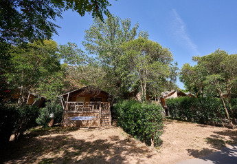 Tienda safari Villatent Nomad entre árboles y arbustos en Camping Les Pêcheurs, Francia, bajo cielo azul.