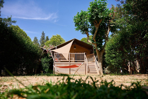 Tienda safari Villatent Nomad en Camping Les Pêcheurs, Francia, rodeada de árboles y hamaca en primer plano.