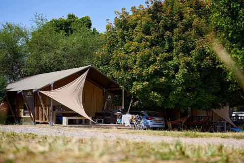 Tenda safari Villatent Nomad al Camping Le Petit Trianon in Francia, circondata da alberi e spazi verdi.