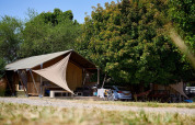Tienda safari Villatent Nomad en Camping Le Petit Trianon en Francia, rodeada de árboles y naturaleza.