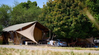 Tienda safari Villatent Nomad en Camping Le Petit Trianon en Francia, rodeada de árboles y naturaleza.