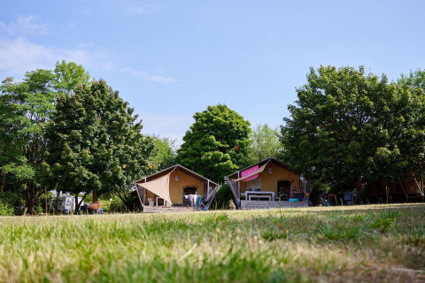 Safaritenten Villatent Nomad op Camping Le Petit Trianon in Frankrijk, omgeven door bomen en grasveld.