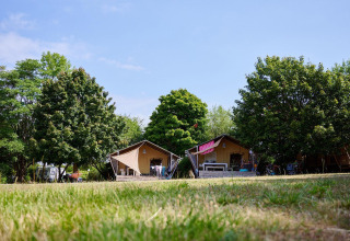Safaritenten Villatent Nomad op Camping Le Petit Trianon in Frankrijk, omringd door bomen en grasveld.