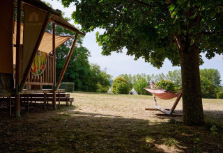 Tienda safari Villatent Nomad en Camping Le Petit Trianon, Francia, con hamaca bajo un árbol y campo abierto.
