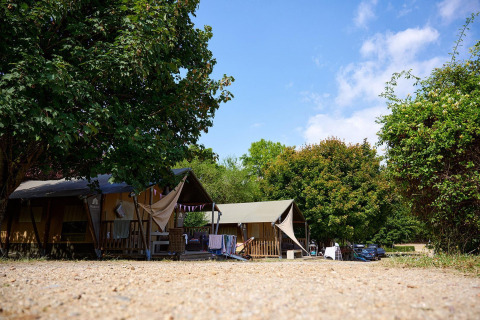 Safaritent Villatent Nomad op Camping Le Petit Trianon in Frankrijk, tussen bomen en enkele auto’s.