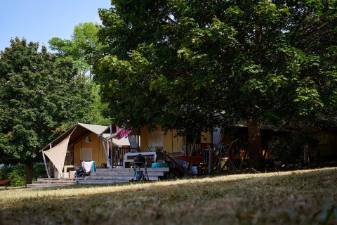 Tienda safari Villatent Nomad en Camping Le Petit Trianon en Francia, rodeada de árboles y naturaleza.