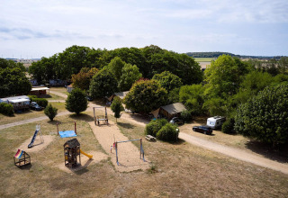 Luftfoto af Camping Le Petit Trianon i Frankrig med Villatent Nomad, legeplads og grønne træer.
