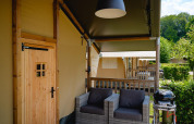 Zona exterior con asientos y barbacoa en una tienda safari Villatent Nomad en Camping 't Geuldal, Países Bajos.