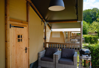 Zona exterior con asientos y barbacoa en una tienda safari Villatent Nomad en Camping 't Geuldal, Países Bajos.