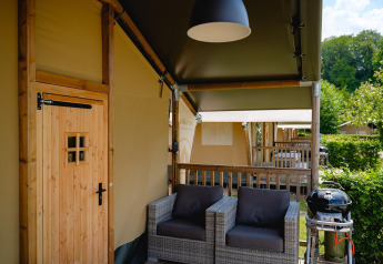 Zona exterior con asientos y barbacoa en una tienda safari Villatent Nomad en Camping 't Geuldal, Países Bajos.