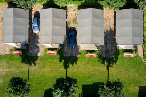 Vista aérea de cuatro tiendas safari y coches en Camping 't Geuldal, Países Bajos, rodeados de césped verde.