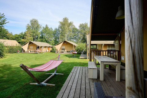 Tiendas safari Villatent Nomad y una hamaca en Camping de Papillon, Países Bajos, rodeadas de césped y árboles.