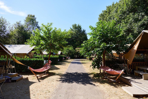Path between Villatent Nomad safari tents with hammocks and trees at Camping Domaine du Logis in France.