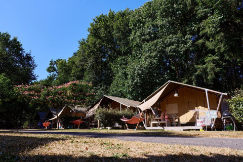 Safari tents at Domaine du Logis campsite in France, featuring hammocks and lush green surroundings.