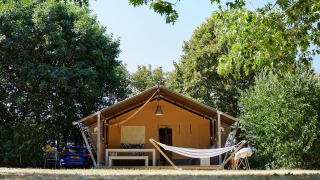 Tienda safari Villatent Nomad con hamaca en Camping La Bretonnière, Francia, rodeada de árboles verdes.