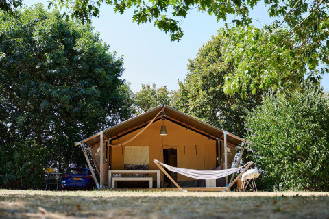 Tienda safari Villatent Nomad con hamaca en Camping La Bretonnière, Francia, rodeada de árboles verdes.