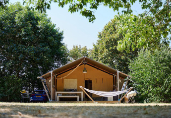 Tienda safari Villatent Nomad con hamaca en Camping La Bretonnière, Francia, rodeada de árboles verdes.