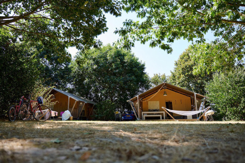 Safari tents, bicycles, and a hammock beneath trees at Camping La Bretonnière in France, Villatent Nomad.