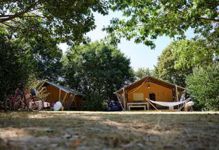 Safari tents, bicycles, and a hammock beneath trees at Camping La Bretonnière in France, Villatent Nomad.