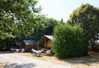 Tiendas tipo safari y hamacas en Camping La Bretonnière en Francia, rodeadas de árboles y vegetación.