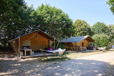 Two safari tents with hammocks at Camping La Bretonnière in France, surrounded by lush green trees.