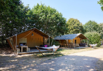 Two safari tents with hammocks at Camping La Bretonnière in France, surrounded by lush green trees.