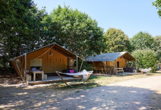 Zwei Safarizelte mit Hängematten auf dem Campingplatz La Bretonnière in Frankreich, umgeben von Bäumen.