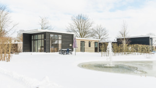 Forest Lodge glamping accommodation in winter, modern cabin with large windows, snow and pond view.