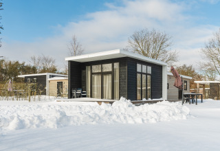 Tiny house Forest Lodge in de sneeuw op Vakantiepark Hölte, Nederland, omgeven door een winterlandschap.